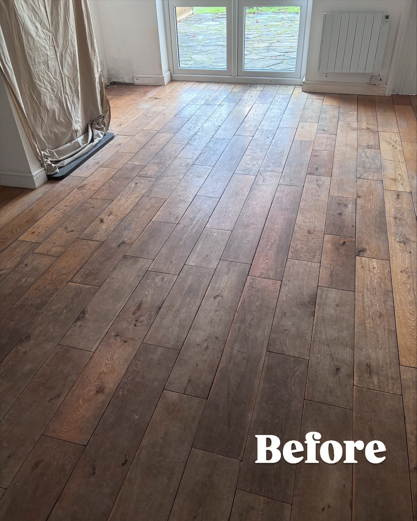 Original dark oak floor in a living room with patio doors before replacement — showing wear and discolouration