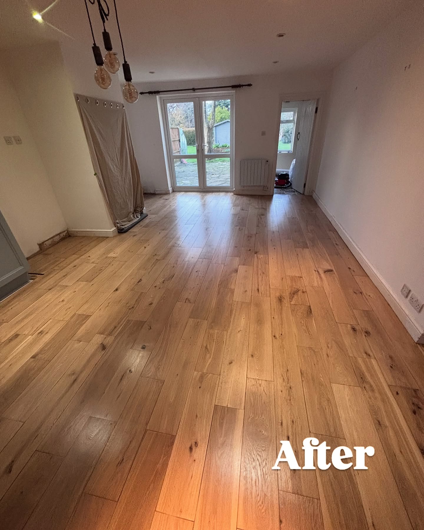 New wide-plank rustic oak flooring installed in a bright living room with patio doors — warm natural tones throughout
