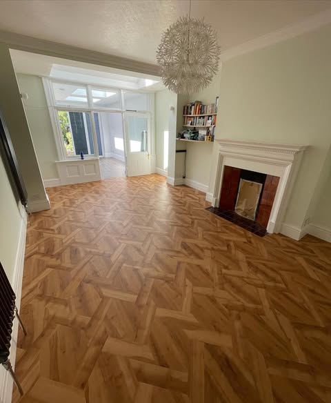 Herringbone oak parquet flooring in a period living room with ornate chandelier, original fireplace and bay window