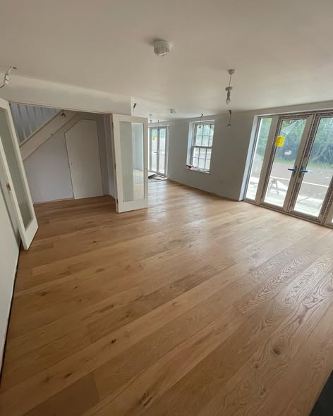 Wide-plank natural oak engineered flooring laid throughout a large bright open-plan ground floor with staircase and French doors to the garden