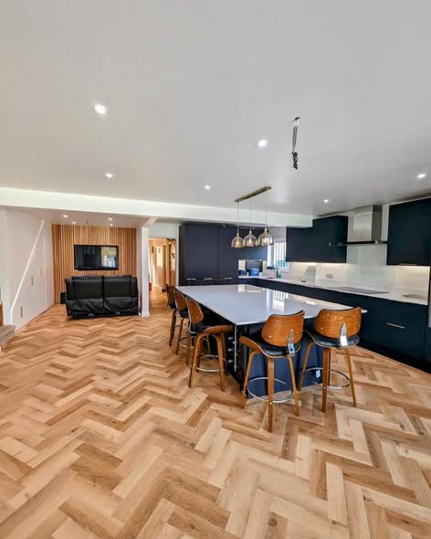 Herringbone natural oak parquet flooring in a spacious open-plan kitchen with dark navy cabinetry, central island and pendant lighting